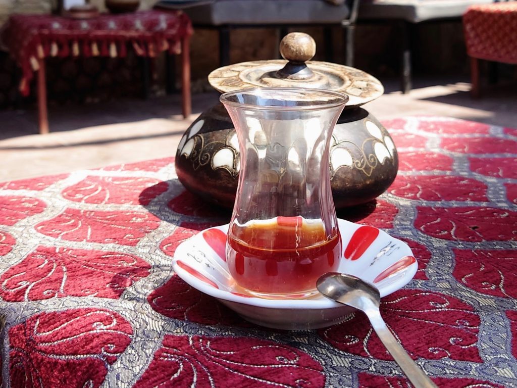 Turkish tea cup with tea and tea pot behind on table with red rug